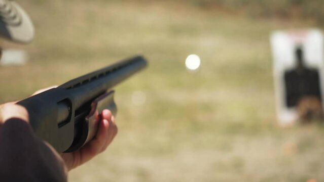 Caucasian man strikes target firing a pump-action shotgun at an outdoor shooting range