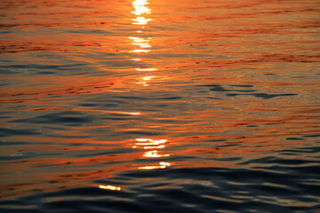 Orange reflections of the setting sun on the wave surface at sunset. Beautiful water background. Sea texture