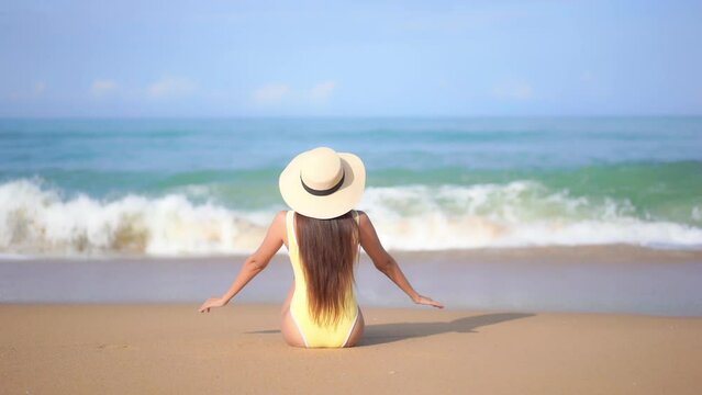 Back of Lonely Woman in Swimsuit Sitting on Sand of Tropical Beach in Front of Sea Waves and Blue Horizon