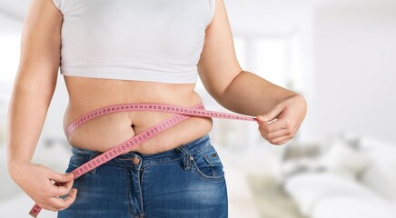 Woman standing showing excessive naked belly, measuring waist with hands, using tape. Body positive, cellulite, obesity, weight control, liposuction.