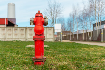 Fototapeta na wymiar Single red fire hydrant on green lawn,blue sky.In a background factory.Autumn,spring,summer day.