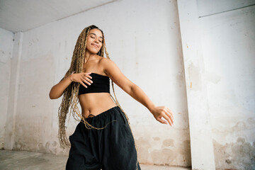 multiracial girl with long blonde braids dancing in a black tracksuit in an abandoned warehouse while smiling and enjoying her passion and exercise.