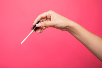 Woman hands holding concealer applicator isolated on pink background