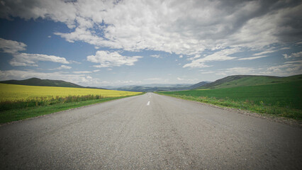 the road leading to the valley of the mountains, through the blossoming yellow fields under the blue sky