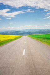 the road leading to the valley of the mountains, through the blossoming yellow fields under the blue sky