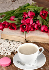 Fototapeta na wymiar Cup of coffee, spoon, book, macaroon, tulips and knitted napkin on wooden table 