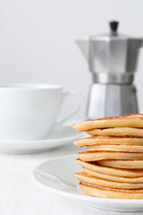 Pancakes on white plate, teacup and coffee maker on white table Selective focus