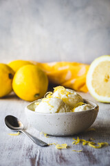 cuenco con bolas de helado de limón sobre una mesa de madera blanca, con limones detrás y espacio en blanco