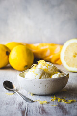 cuenco con bolas de helado de limón sobre una mesa de madera blanca, con limones detrás y espacio...