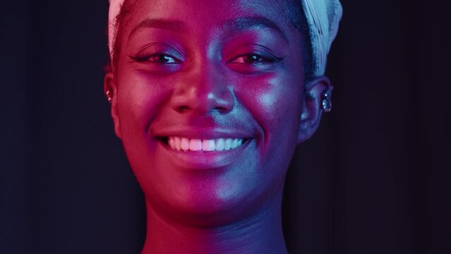 Native African American woman portrait. Female person smiling, looking in camera. Happy face in neon light, pretty latin model with wide smile posing on black background. 