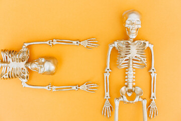 Creative Halloween composition with golden skeletons over orange background. Funny Halloween concept