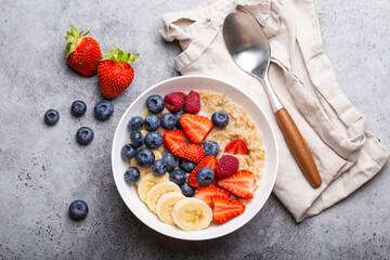 Oatmeal porridge with fruit and berries in bowl with spoon on gray stone background table top view,...