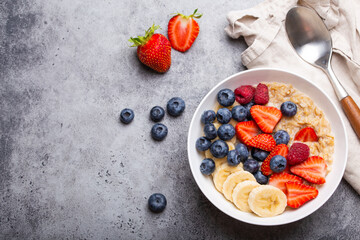 Oatmeal porridge with fruit and berries in bowl with spoon on gray stone background table top view,...
