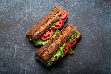 Two dark ciabatta sandwiches with green salad, ripe red tomatoes, onion and tuna on rustic concrete stone background top view. Vegetable vegetarian sandwiches, healthy snack or lunch