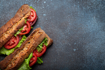 Two dark ciabatta sandwiches with green salad, ripe red tomatoes, onion and tuna on rustic concrete stone background top view. Vegetable vegetarian sandwiches, healthy snack or lunch. Space for text