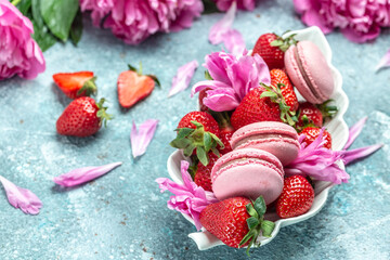 Pink peony rose flower and macaroni cookies and sweet strawberry on blue background. Small French cakes Macarons with fruit. top view