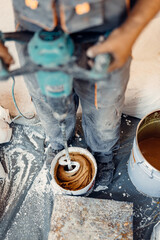 Professional worker mixes two chemical compounds in the metal bucket using the mixer