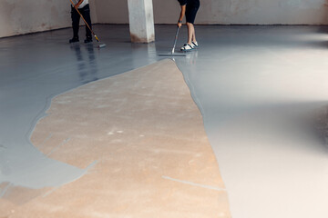 A construction worker apply grey epoxy resin in an industrial hall