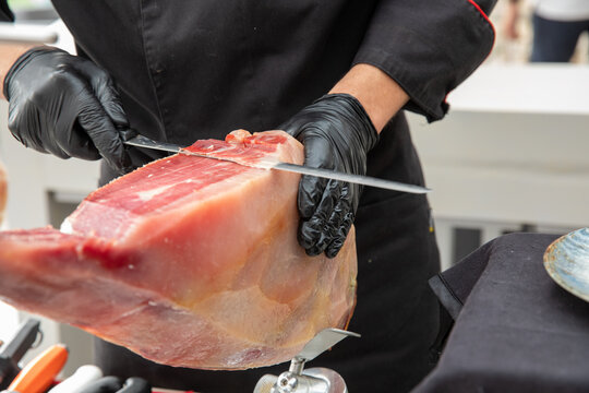Professional ham slicer cutting an Iberian ham with a long knife and black gloves.