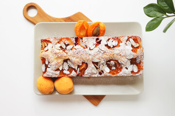 rectangular mouth-watering homemade apricot pie on a rectangular plate, on a wooden cutting board. Daylight, white background, top view