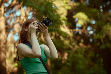 Red haired beauty girl enjoys nature and takes photos. Young woman wearing green top.