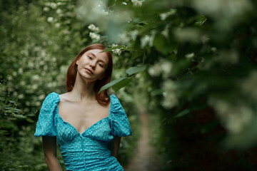 Pretty young woman posing for the camera in the forest. The girl is wearing a blue dress, she is looking at the camera.