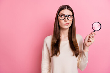 Portrait of attractive suspicious girl using loupe copy space ad isolated over pink pastel color background