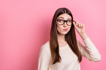 Portrait of attractive suspicious girl touching specs looking copy space solution isolated over pink pastel color background
