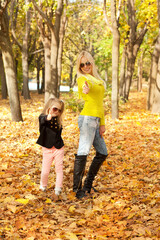 Young mother and little daughter playing fashion dressed in sunglasses in autumn park.