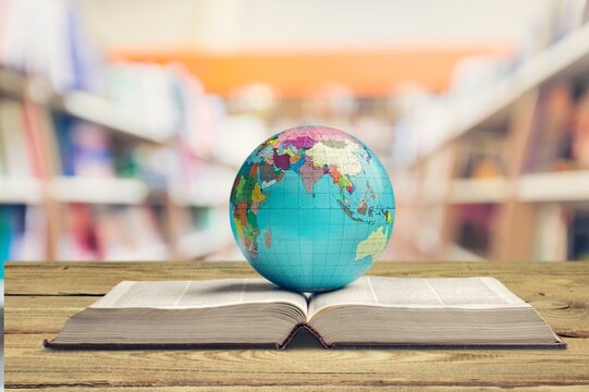 Old globe lying on an open book against the background of bookshelves in a library. Science, education, travel. Education history and geography team.