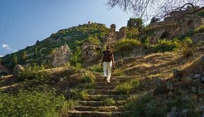 Tourist man with backpack exploring ruins of old city of Mystras, UNESCO world heritage archeological sight.
