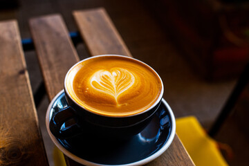 Black cup of cappuccino with latte art on wooden background.