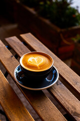 Black cup of cappuccino with latte art on wooden background.