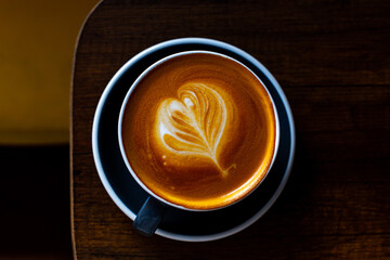Black cup of cappuccino with latte art on wooden background.