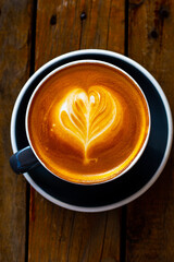 Black cup of cappuccino with latte art on wooden background.
