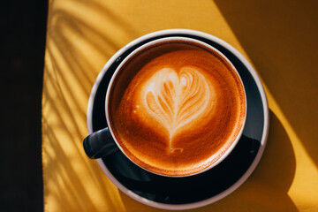 Black cup of cappuccino with latte art on yellow sofa background.