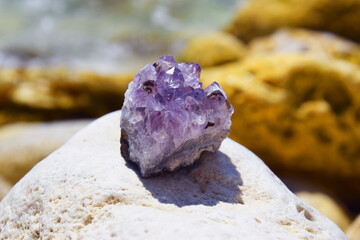 A beautiful amethyst druze lies on a stone against the backdrop of the sea. A splice of purple...