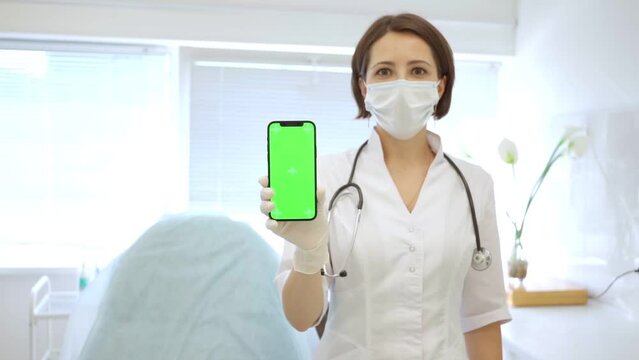 beautiful cute doctor in medical mask in medical office holds smartphone with chroma key in her hand. general practitioner. Doctor female dermatologist cosmetologist. 