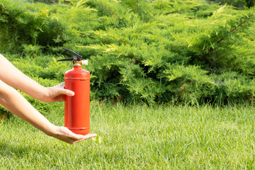 a fire-extinguisher is red in woman hands on a green lawn