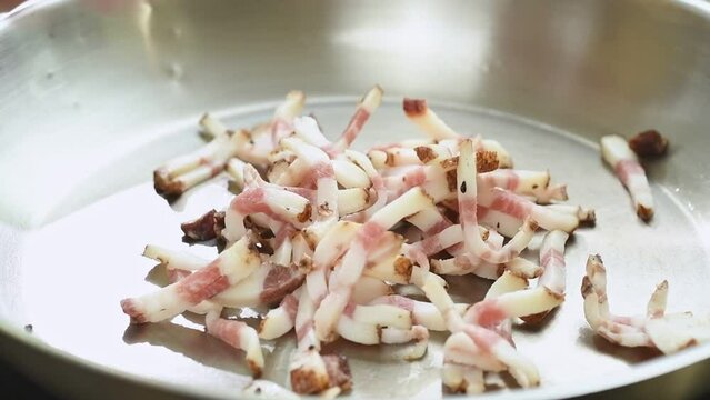 Putting of pieces guanciale in a frying pan.
