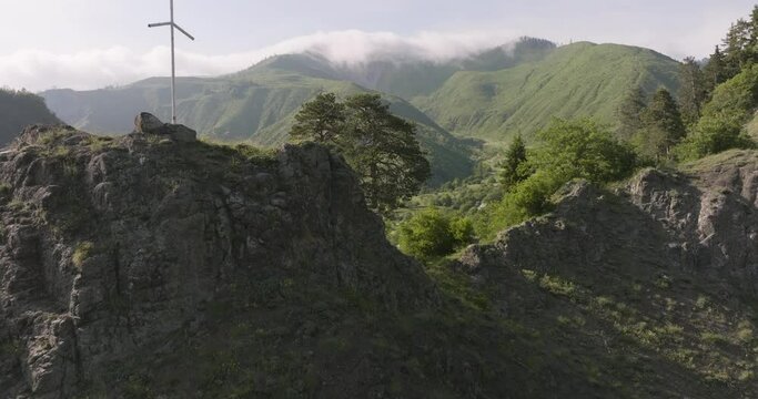 White Grapevine Cross On Rocky Clifftop With Daba Settlement On A Sunny Summer Day In Georgia. - aerial reveal