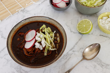 Vegan Pozole Rojo with toppings: shredded ice lettuce, radish and white onion. Mexican cuisine dish...