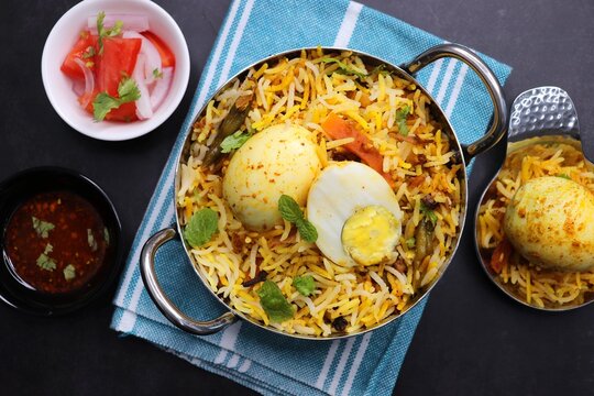 Egg dum Biryani or anda biryani Fragrant Basmati rice cooked with spicy masala gravy along with spices, veggies and boiled eggs. served with yogurt, salad and salan. Black background with copy space.