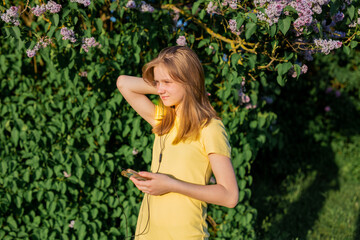 teenage girl in a yellow dress listens to music and holds a phone in her hands