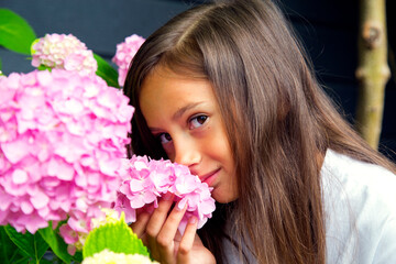 Fototapeta premium Portrait of a little beautiful girl with a bouquet of hydrangeas in her hands. Child girl smells hydrangea flowers. The concept of childhood, happiness, carelessness and nature.