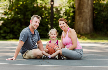 Happy family and child daughter outside at basketball court.