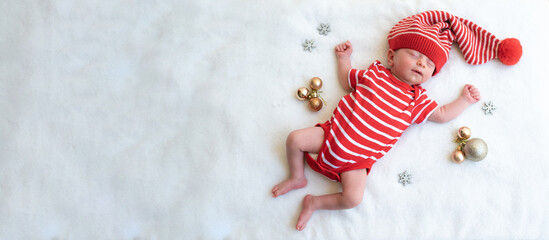 Fototapeta na wymiar Baby in red Santa hat decorate by golden ball. Newborn sleeping peacefully on white blanket with hands up. Happy new year and Christmas. Top view. funny elf and fairy. space for text