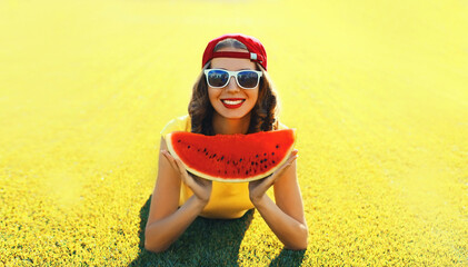 Summer portrait of happy smiling young woman eating fresh juicy slice of watermelon on the grass in the summer park