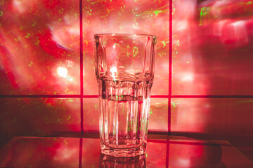 Crystal glass for cocktails with water on the glass surface. Abstract background with red smoke light.