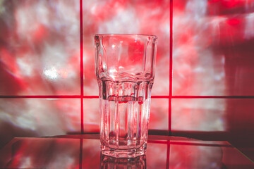 Crystal glass for cocktails with water on the glass surface. Abstract background with red smoke light.